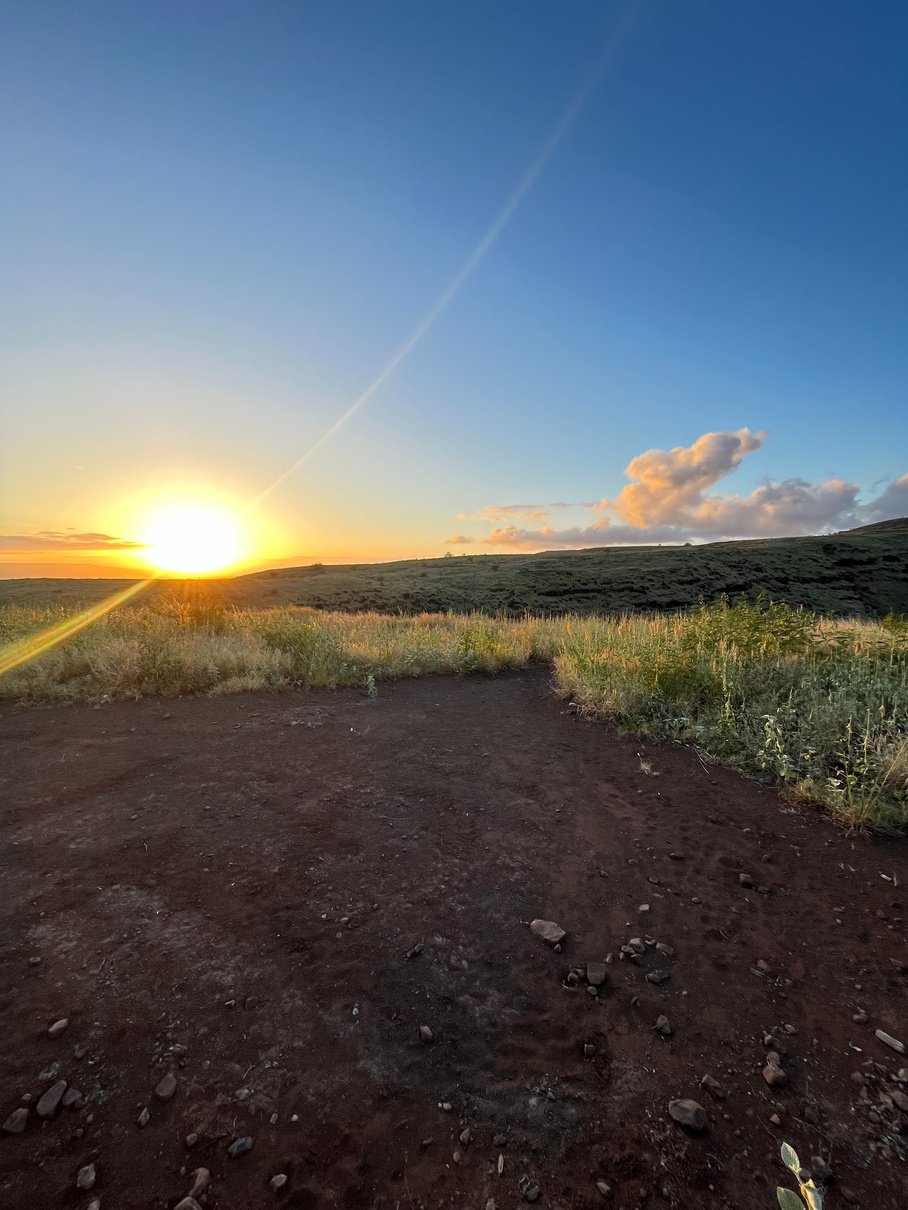 the sun is setting over a dirt road in the middle of a field axis deer hunt molokai